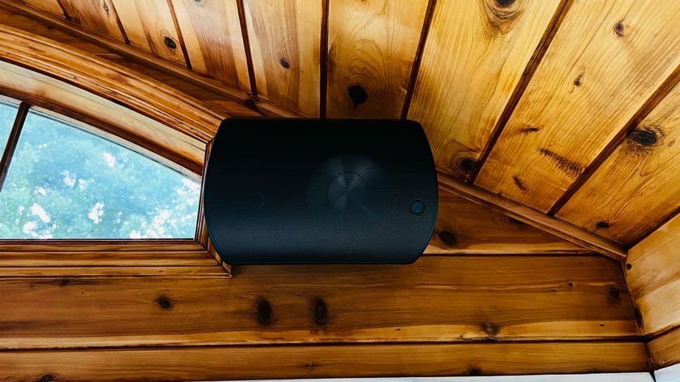 Black outdoor speaker mounted in the peak of a covered cedar ceiling