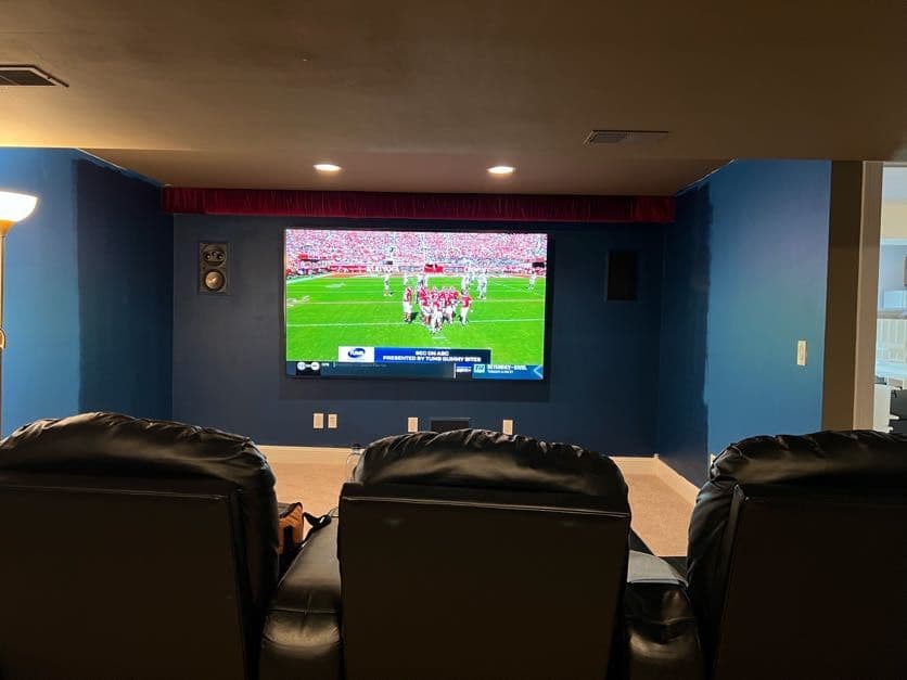 Blue home theater room with in-wall speakers, recliner seating, and live football on screen