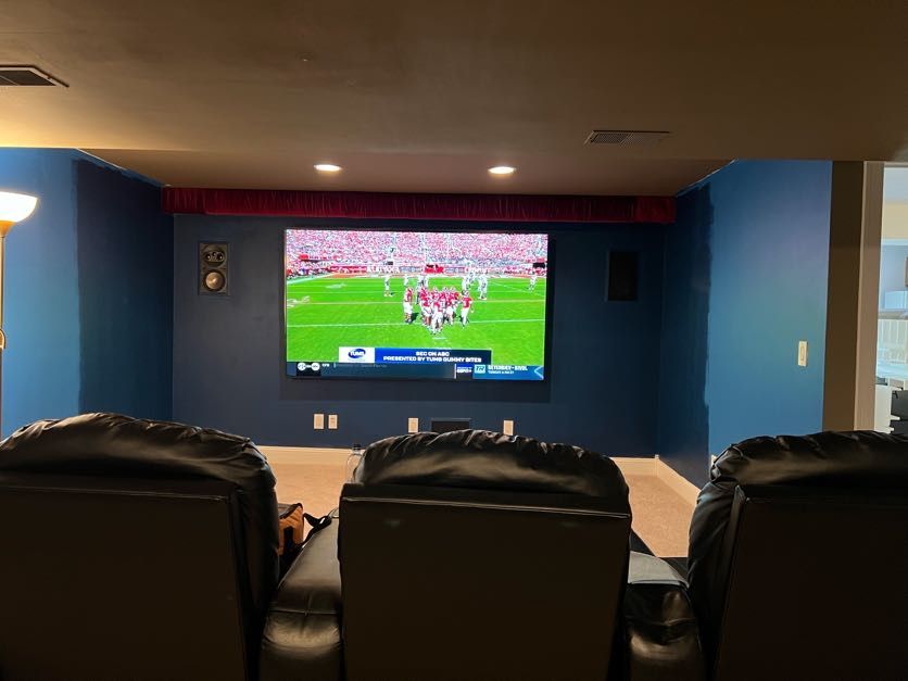 Blue home theater room with in-wall speakers, recliner seating, and live football on screen