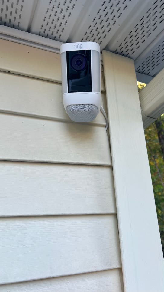 White Ring spotlight camera mounted under an eave on light siding